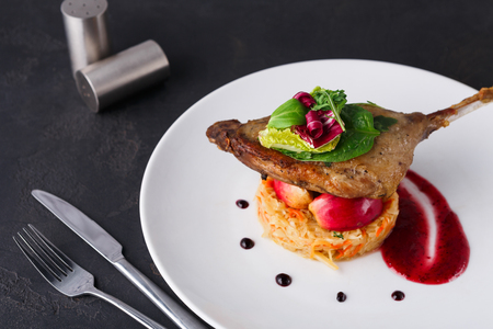 Exclusive restaurant meals. Duck confit with braised cabbage, baked apple and cranberry sauce served on snow white plate on black table background, copy spaceの写真素材