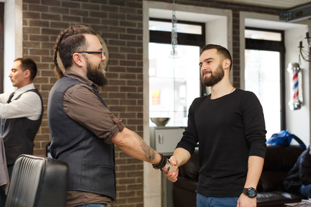 Thankful client and barber shaking hands after haircut. Hairstylist and satisfied customer handshaking at barbershopの写真素材