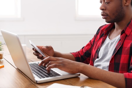 African-american businessman working with mobile and laptop in modern office, crop.の写真素材