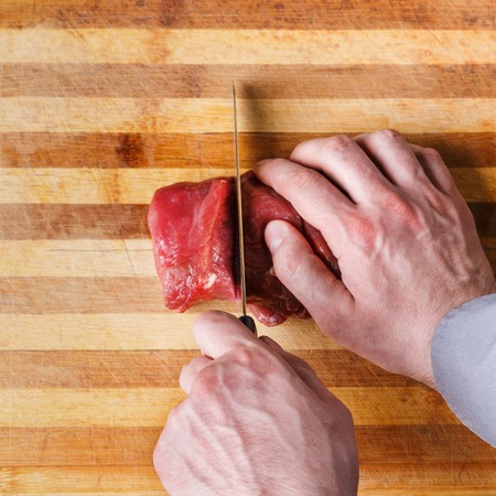 Man cutting filet mignon in pieces. Chef preparing fresh meat for cooking on wooden board at restaurant kitchen. Modern cuisine backgroung with copy space, top viewの写真素材