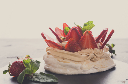 Fitness restaurant dessert at black and white background. Anna Pavlova meringue with low-fat whipped cream and fresh strawberry on slate and cake spatula aside, closeup, copy spaceの写真素材