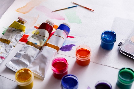 Artist workplace. Set of color gouache jars, acrylic and oil paints and brushes on white wooden desk background, copy spaceの写真素材