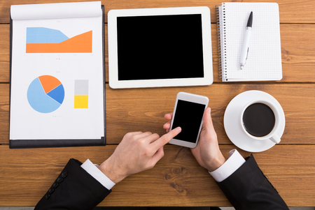 Businessman using phone at workplace. Man working with portable computer, copy space on display, top view, close upの写真素材