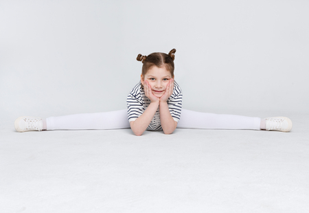 Happy girl sitting in splits on white background. Cute little gymnast doing exercises at studio, copy spaceの写真素材