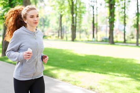 Young sporty woman running in green park during morning workout, copy space