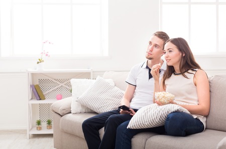 Smiling young couple relaxing and watching TV at home, having rest after hard week, copy spaceの写真素材
