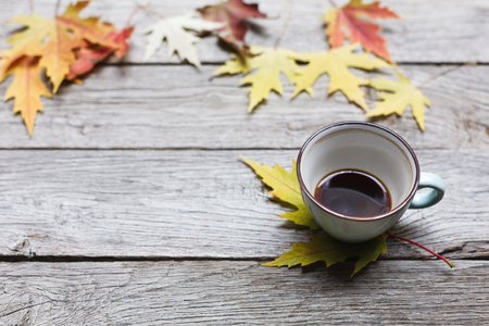 Autumn leaves and black coffee composition. Blue coffee cup half empty at weathered rustic wood background with copy space. Fall hot drinks conceptの写真素材
