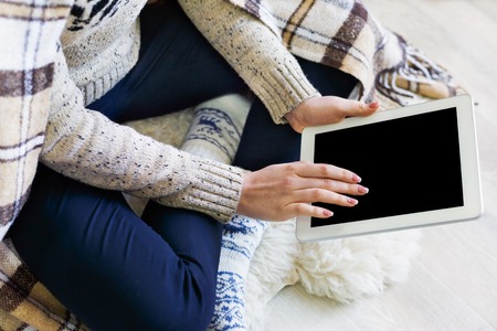 Winter online shopping. Female buyer touch screen of tablet with copy space. Woman in checkered plaid, buy presents, prepare to xmas in cozy home interior. Winter salesの写真素材