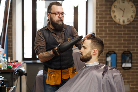 Man getting haircut by hairstylist at barbershop. Stylish barber and clientの写真素材