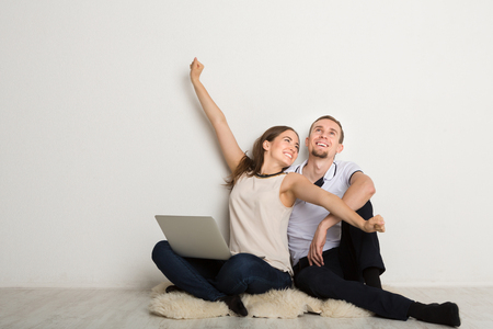 Cheerful couple using laptop at home, sitting on floor in empty room, copy spaceの写真素材