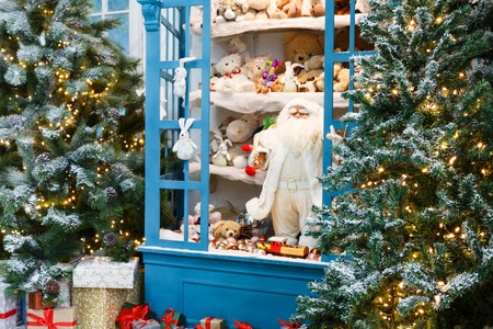 Christmas magical atmosphere background. Modern interior design for winter holidays. Pine trees decorated with shining lights, showcase with toys and present boxesの写真素材