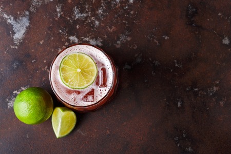 Red cocktail on brown background. Refreshing alcohol drink with tequila, citrus juice, ice and lime on dark marbled table, copy space, top viewの写真素材