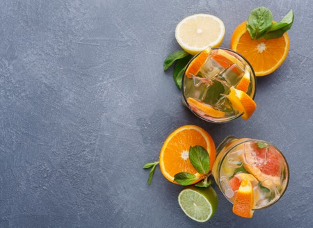 Summer citrus drinks background. Detox water in glasses and tropical fruits variety on gray table. Colorful backdrop top view, copy space. Bar beverages or healthy eating dietary conceptの写真素材