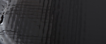 Abstract black textured background closeup. Wavy surface reflecting light