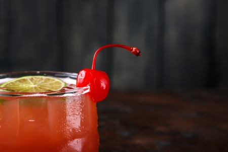 Red cocktail at wooden background. Refreshing alcohol drink with tequila, citrus juice, ice and lime on brown marbled table, copy space, closeup, selective focusの写真素材