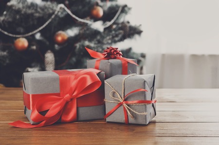 Christmas gifts decorated with red ribbon on table, closeup, selective focus. Christmas tree background.の写真素材