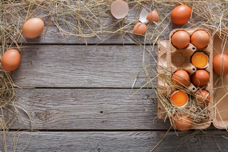 Fresh chicken eggs background. Brown and white eggs in craft carton pack on hay at rustic wood table with copy space. Top view. Natural healthy food and organic farming concept.の写真素材