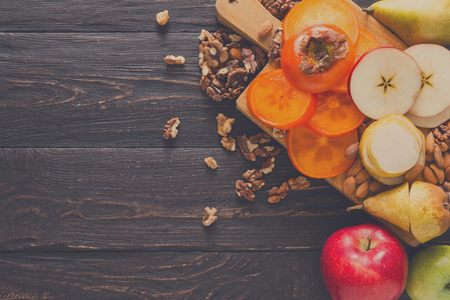 Healthy food - wood board with cut organic raw fruits on wooden background. Top view of sliced ingredients for fruit salad or snack - apple, pear, nuts, persimmon. Flat lay, copy spaceの写真素材