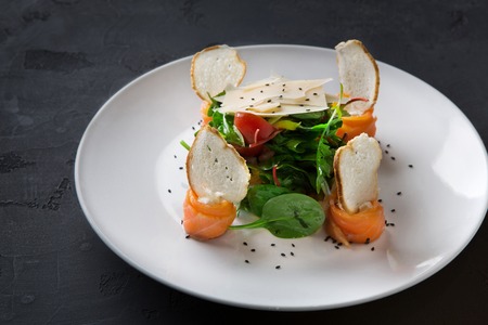 Restaurant dish on white plate on black background. Salad with spinach, arugula and cheese decorated...