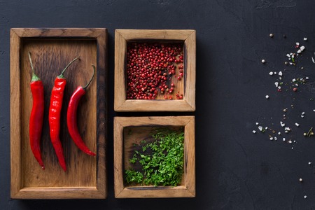 Spices and chilli in wooden boxes on black background. Pepper and parsley on dark background, copy...