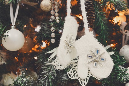 Winter holidays atmosphere background. Closeup of beautifully decorated fir tree with modern shiny baubles, beards, garland and small knitted mittens . Christmas and new year magic at homeの写真素材