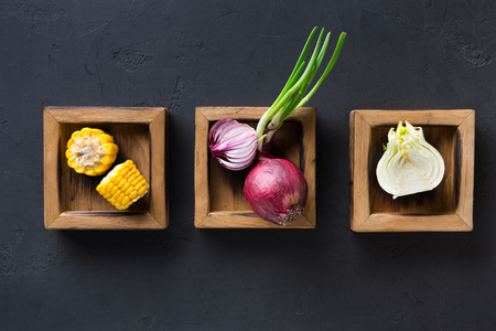 Cooking ingredients for restaurant dish on black background. Wooden boxes with onions and corn, top viewの写真素材