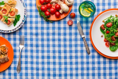 Healthy eating concept. Fresh salad with greens, tomatoes and mushrooms, casserole and lemonade on checkered tablecloth background. Organic vegetables top view, copy space.の写真素材