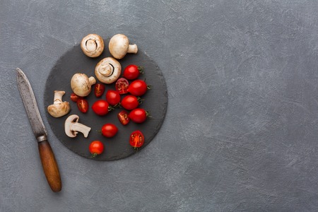 Cut tomatoes and mushrooms on rustic slate stone plate. Cooking healthy food on gray background, copy space, top view.の写真素材