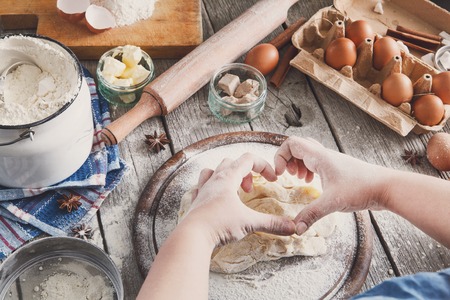 Baking concept. Flour, milk, butter, yeast and eggs carton on rustic wooden table, cooking ingredients. Unrecognizable womans hands pov view knead dough. Female chefの写真素材