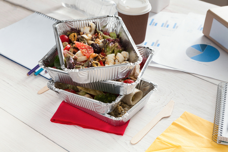 Healthy daily meals delivery at office table, coffee take away cup and vegetable salads in foil containers on white wooden desk. Snack at break timeの写真素材