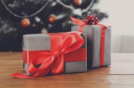 Christmas gifts decorated with red ribbon on table, closeup, selective focus. Christmas tree background.の写真素材