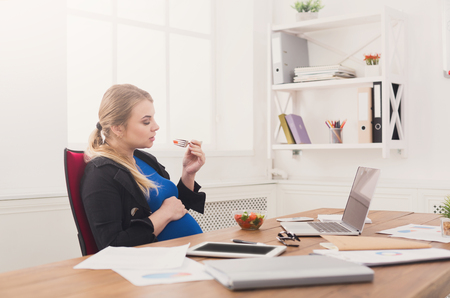 Pregnant businesswoman eating salad at office. Side view on relaxed expectant business lady having healthy lunch at workplace, copy spaceの写真素材