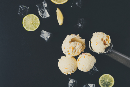 Ice cream scoops with ice cubes and lemon slices and scoop on black background. Delicious cold sweet dessert, copy spaceの写真素材