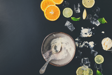 Empty bowl of ice cream with lemon and orange slices, ice cubes and mint on black background, messy dining placeの写真素材