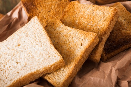 Toasted slices of white bread in craft paper on wooden table. Still life, food background, closeup