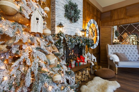 Beautiful christmas interior. Warm room with fireplace, decorated christmas tree, lots of presents and huge clock on wooden wall. Cozy home for winter holidays, copy space, side viewの写真素材