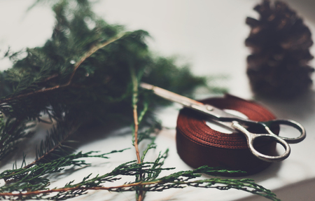 Gift wrapping closeup background. Ribbon for packaging christmas present boxes, thuja tree branches, pine cones and scissors. Christmas and winter holidays concept. Selective focusの写真素材