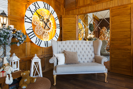 Beautiful holdiay living room. Big magical clock on wooden wall and soft cozy gray couch. Winter holiday design and decorations backgroundの写真素材