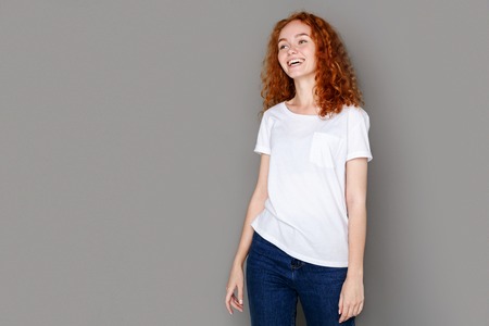 Laughing redhead beauty. Cheerful girl in casual clothes posing at studio on gray background, copy...