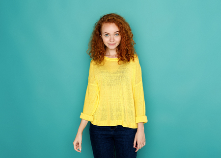 Confident redhead beauty. Cheerful girl in casual clothes posing at studio on blue background, copy spaceの写真素材