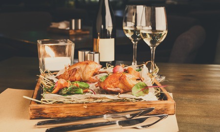 Romantic dinner at gourmet cuisine restaurant. Quails with asparagus and chanterelles served on grungy wooden platter, wine glasses and a candle on table. Exclusive meals for a foodie, copy spaceの写真素材