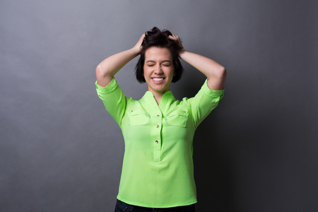 Feeling playful. Excited woman in casual outfit closed eyes and touching hair, gray studio backgroundの写真素材