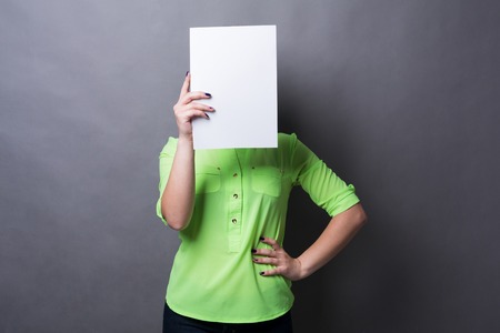 Young woman with blank white paper at face. Serious girl covering her head with advertising sheet, copy spaceの写真素材