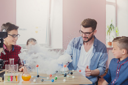 Stem education. Group of kids with teacher doing chemical experiment with liquid nitrogen in laboratory, copy space. Early development conceptの写真素材