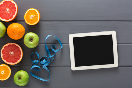 Grapefruitt, orange, apple and blank tablet with measuring tape on gray background copy space. Diet, healthy eating, slimming conceptの写真素材