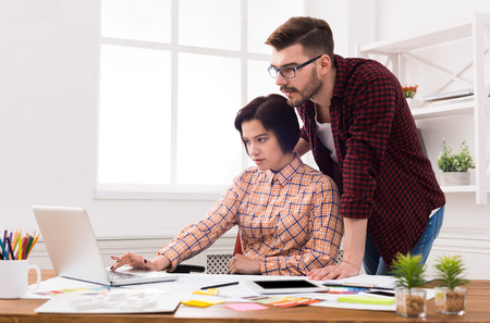 Couple of young designers working at modern office. Two coworkers discussing startup project over laptopの写真素材