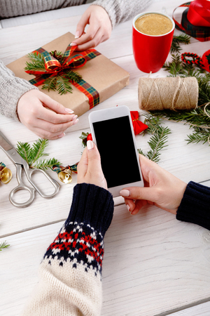 Christmas online shopping background. Cell phone screen with copy space on white wooden table, credit card and present. Mobile applications and internet commerce on winter holidays conceptの写真素材