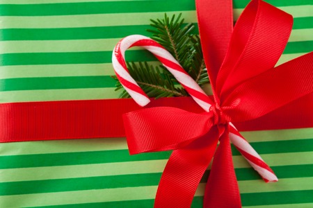 Closeup of handmade present box. Gift in striped green wrapping paper, decorated with red satin ribbon bow and candy cane lollipop, top viewの写真素材