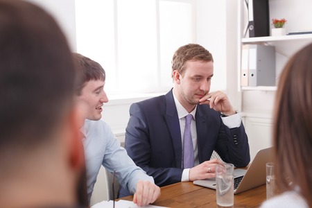Business team meeting. Young successful emploee in official suit reading report at laptop. White...