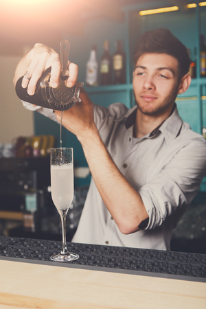 Young handsome bartender in bar interior pouring alcohol cocktail drink into glass. Service industry occupation.の写真素材